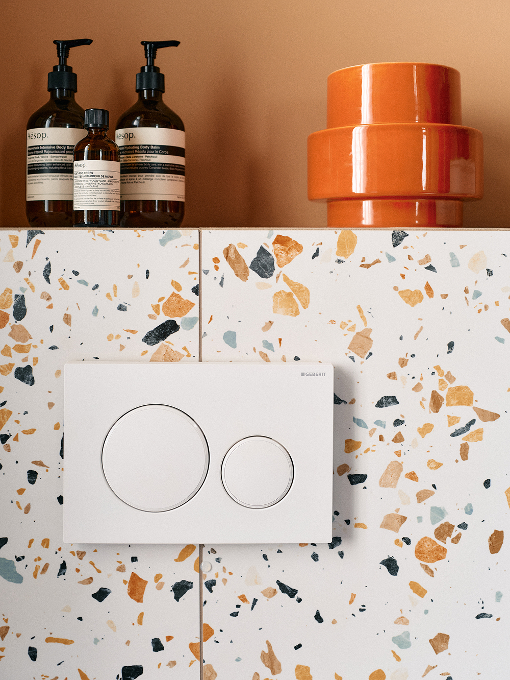 Terrazzo-Wand mit Pflegeprodukten und orangefarbener Vase
